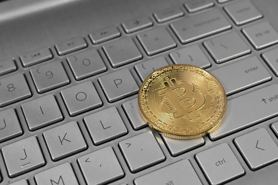 Gold-colored physical Bitcoin token resting on a silver laptop keyboard.